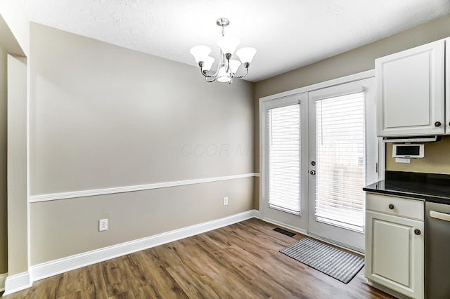 unfurnished dining area with an inviting chandelier, hardwood / wood-style floors, and french doors