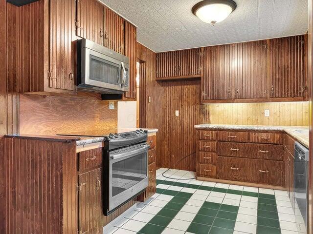 kitchen featuring light tile patterned floors, appliances with stainless steel finishes, and wooden walls