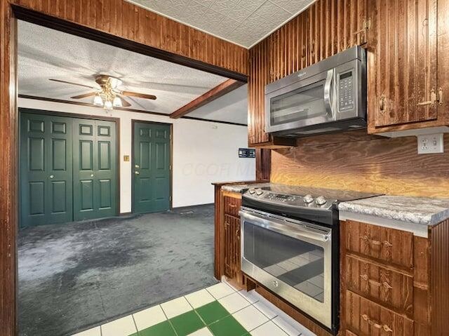 kitchen featuring ceiling fan, wooden walls, stainless steel appliances, ornamental molding, and light carpet