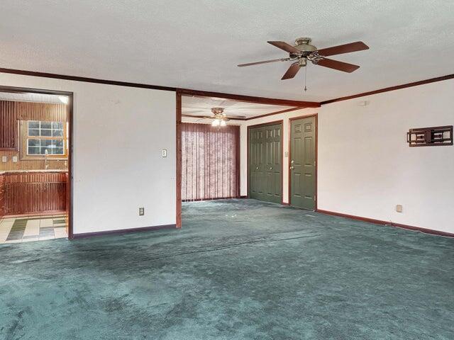 carpeted empty room with ceiling fan, sink, a textured ceiling, and crown molding