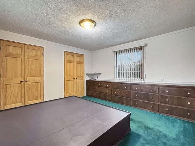 unfurnished bedroom with a textured ceiling, crown molding, and dark colored carpet