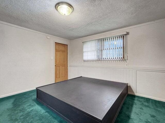 unfurnished bedroom featuring a textured ceiling, dark colored carpet, and crown molding