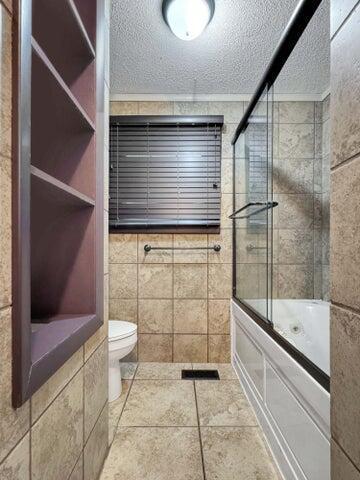 bathroom featuring a textured ceiling, toilet, tile walls, and combined bath / shower with glass door