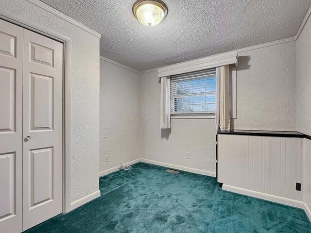 carpeted empty room with a textured ceiling and ornamental molding