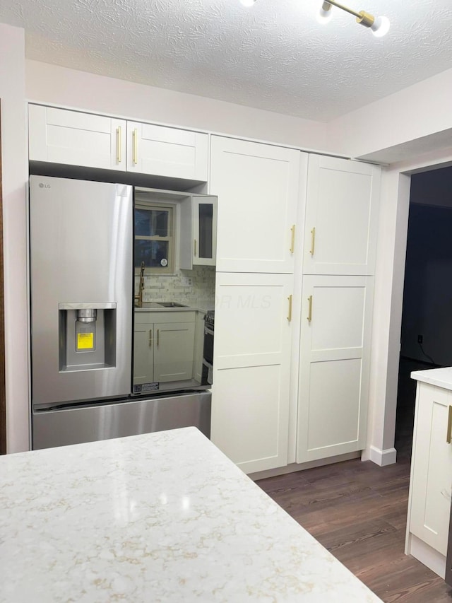 kitchen with dark wood-type flooring, light stone counters, white cabinetry, and stainless steel fridge