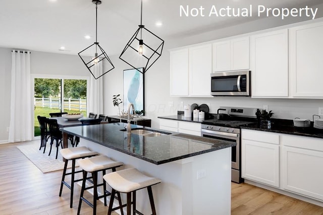 kitchen with a sink, light wood-style floors, appliances with stainless steel finishes, dark stone counters, and a center island with sink