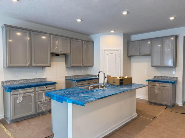 kitchen featuring dark countertops, an island with sink, a sink, and recessed lighting