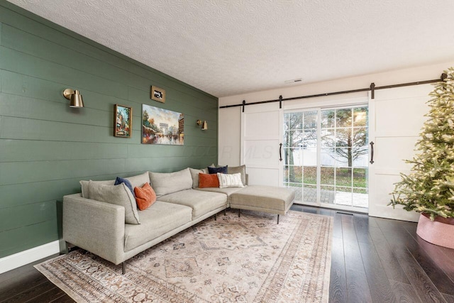 living room with a barn door, wood walls, wood-type flooring, and a textured ceiling