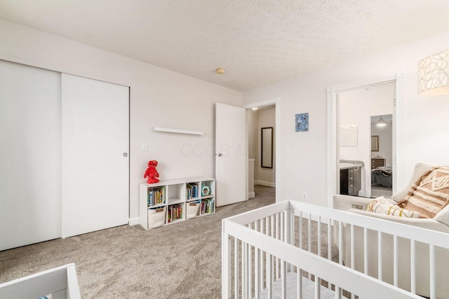 carpeted bedroom featuring ensuite bathroom, a crib, a textured ceiling, and a closet