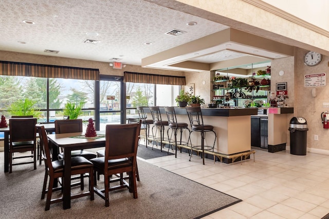 dining space with light tile patterned floors, a textured ceiling, bar, and a healthy amount of sunlight