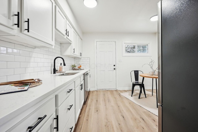 kitchen with dishwasher, sink, tasteful backsplash, white cabinets, and light wood-type flooring