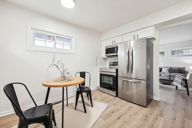 kitchen with backsplash, stainless steel appliances, white cabinetry, and light hardwood / wood-style floors