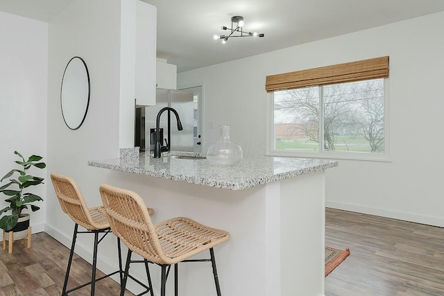 kitchen featuring kitchen peninsula, a kitchen breakfast bar, dark hardwood / wood-style flooring, sink, and white cabinets