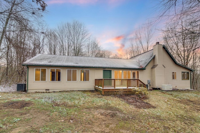 back house at dusk featuring a yard, a wooden deck, and central air condition unit