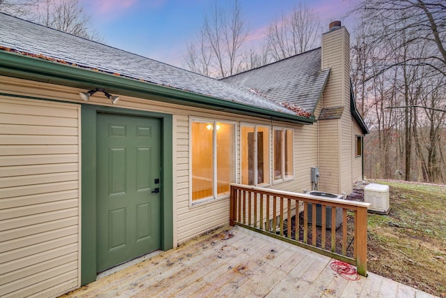 exterior entry at dusk with a wooden deck and central air condition unit