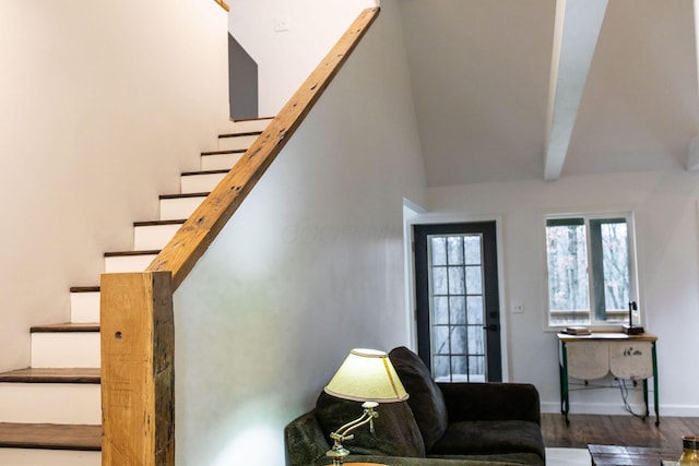 staircase featuring a towering ceiling, beamed ceiling, and wood-type flooring