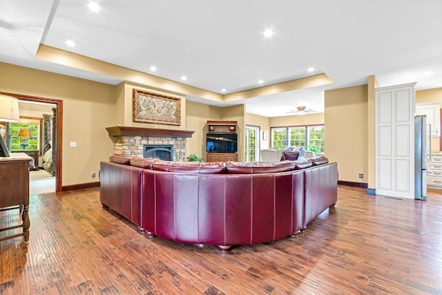 living room with hardwood / wood-style flooring, a stone fireplace, ceiling fan, and a tray ceiling