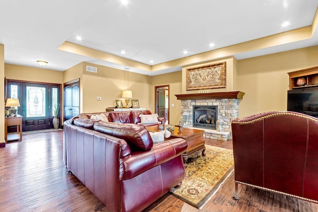 living room featuring a raised ceiling, a fireplace, and wood-type flooring