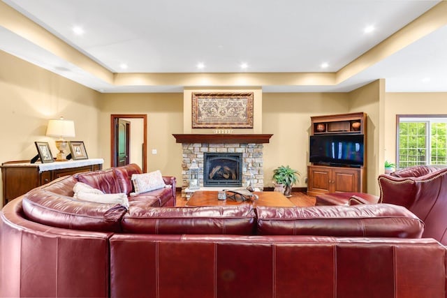 living room featuring a tray ceiling and a stone fireplace