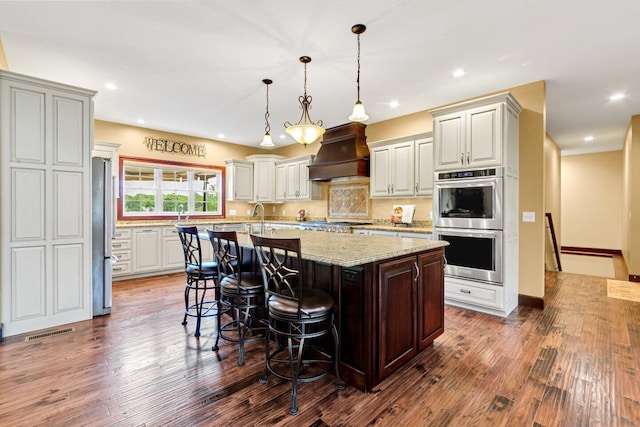 kitchen with a kitchen breakfast bar, dark hardwood / wood-style floors, light stone countertops, an island with sink, and custom range hood