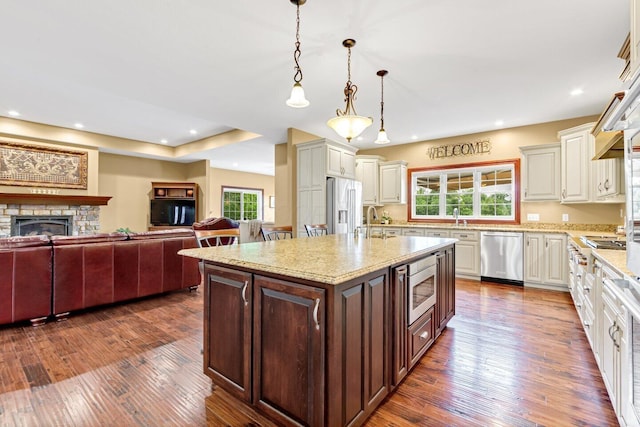 kitchen with appliances with stainless steel finishes, a kitchen island with sink, dark wood-type flooring, a healthy amount of sunlight, and hanging light fixtures