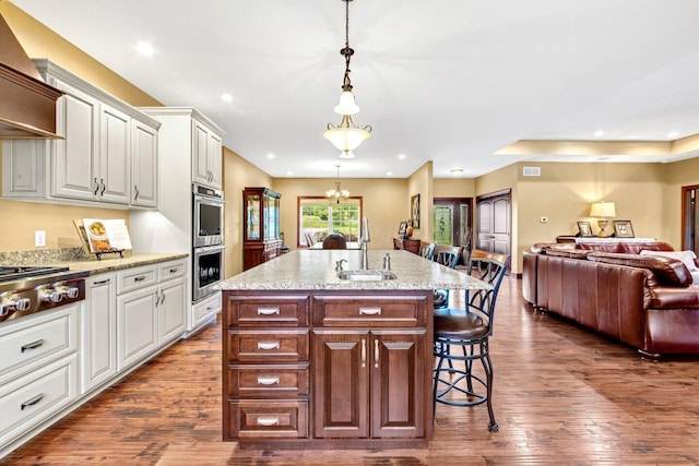 kitchen with a kitchen breakfast bar, dark hardwood / wood-style flooring, white cabinets, and an island with sink