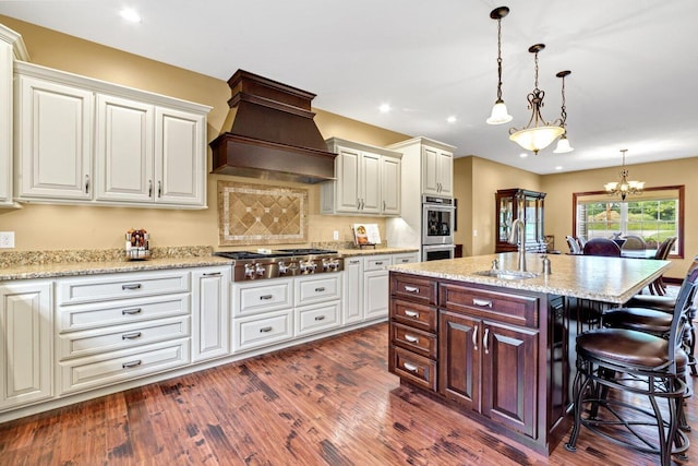 kitchen with a kitchen bar, stainless steel appliances, sink, decorative light fixtures, and an island with sink