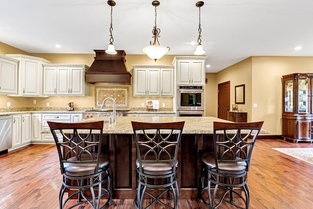 kitchen with light stone counters, light hardwood / wood-style flooring, decorative light fixtures, a kitchen island with sink, and appliances with stainless steel finishes