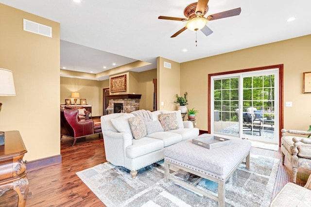 living room featuring hardwood / wood-style flooring, ceiling fan, and a stone fireplace