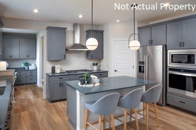 kitchen with stainless steel appliances, gray cabinetry, hanging light fixtures, a kitchen island, and wall chimney exhaust hood