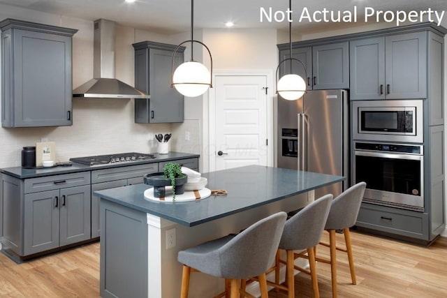 kitchen featuring appliances with stainless steel finishes, wall chimney exhaust hood, hanging light fixtures, and gray cabinets