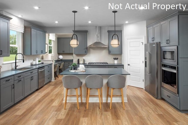 kitchen featuring stainless steel appliances, gray cabinetry, decorative light fixtures, wall chimney range hood, and sink