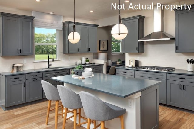 kitchen with wall chimney range hood, sink, light hardwood / wood-style flooring, hanging light fixtures, and gray cabinetry