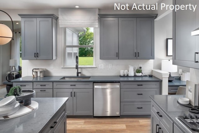 kitchen with dark stone countertops, stainless steel dishwasher, sink, light hardwood / wood-style flooring, and gray cabinetry