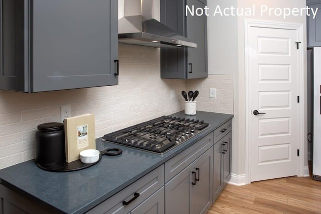 kitchen featuring stainless steel gas stovetop, gray cabinets, decorative backsplash, wall chimney range hood, and light hardwood / wood-style flooring