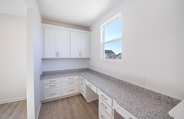 unfurnished office with built in desk, light wood-style flooring, and baseboards