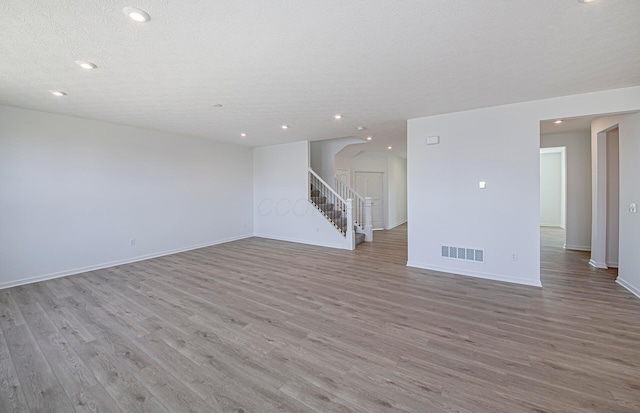 spare room with stairs, wood finished floors, visible vents, and a textured ceiling