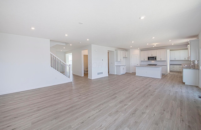 unfurnished living room with visible vents, recessed lighting, light wood finished floors, baseboards, and stairs