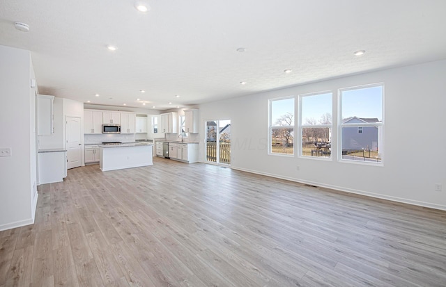 unfurnished living room with visible vents, baseboards, recessed lighting, light wood-style flooring, and a sink