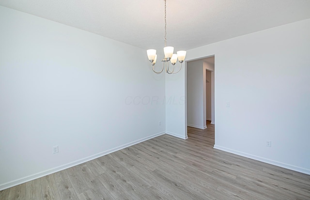 empty room with a textured ceiling, light wood-style flooring, baseboards, and a chandelier