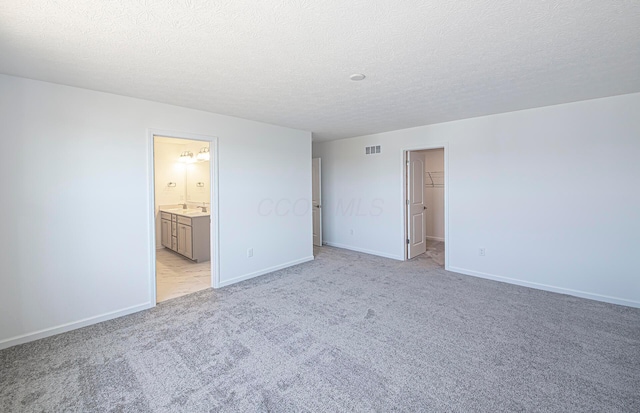 unfurnished bedroom with baseboards, visible vents, a sink, a spacious closet, and light carpet