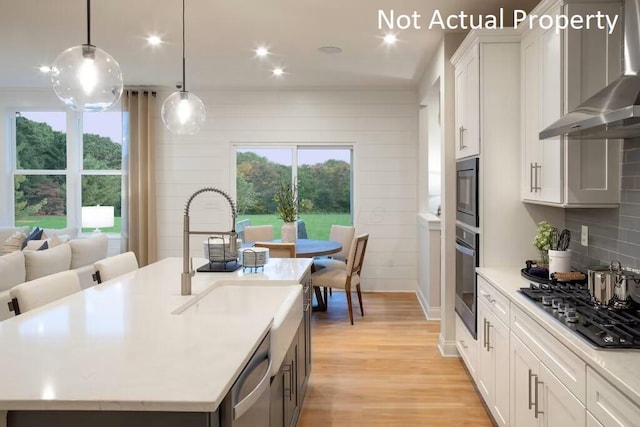 kitchen featuring white cabinetry, an island with sink, decorative light fixtures, and wall chimney exhaust hood