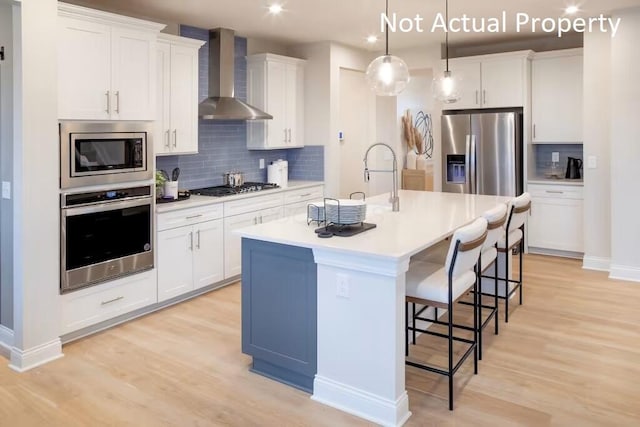 kitchen with appliances with stainless steel finishes, a kitchen island with sink, wall chimney range hood, and white cabinets