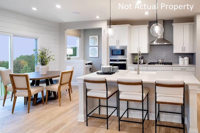 kitchen featuring appliances with stainless steel finishes, pendant lighting, wall chimney range hood, and white cabinets