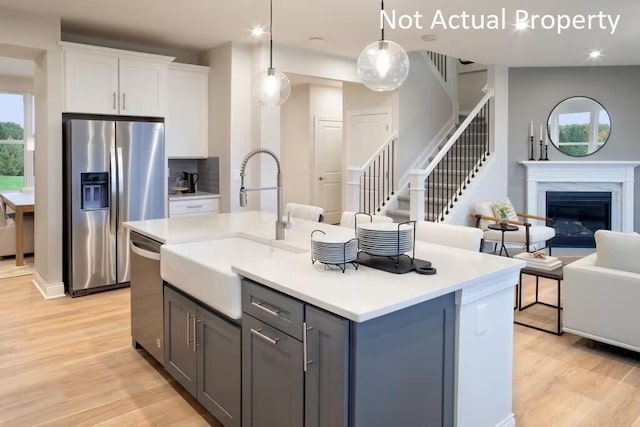 kitchen with appliances with stainless steel finishes, decorative light fixtures, white cabinetry, gray cabinetry, and a center island with sink