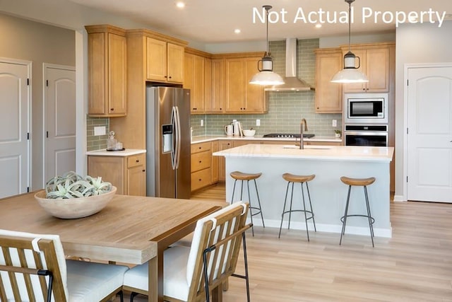 kitchen with pendant lighting, wall chimney exhaust hood, stainless steel appliances, backsplash, and light hardwood / wood-style flooring