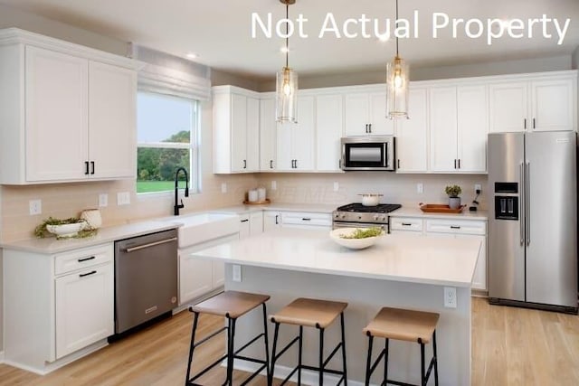 kitchen featuring decorative light fixtures, light hardwood / wood-style floors, a center island, stainless steel appliances, and white cabinets