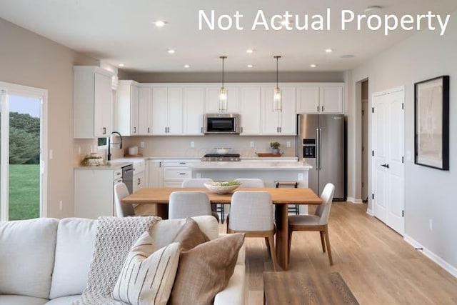 kitchen featuring stainless steel appliances, light hardwood / wood-style floors, white cabinetry, and decorative light fixtures