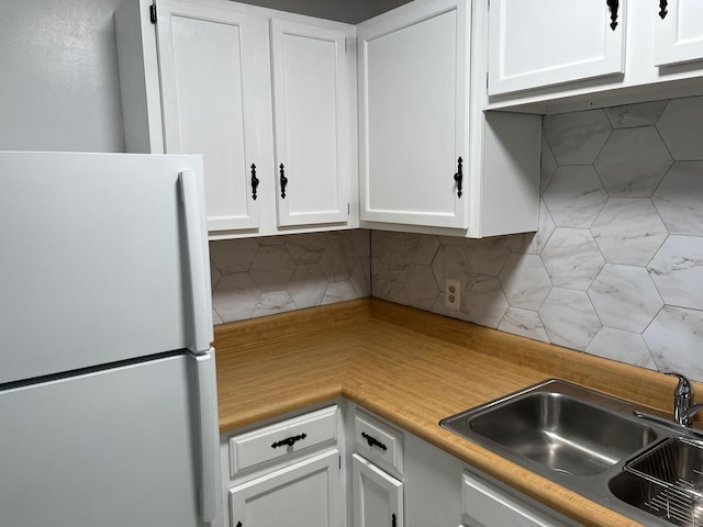 kitchen with white cabinets, decorative backsplash, white fridge, and sink