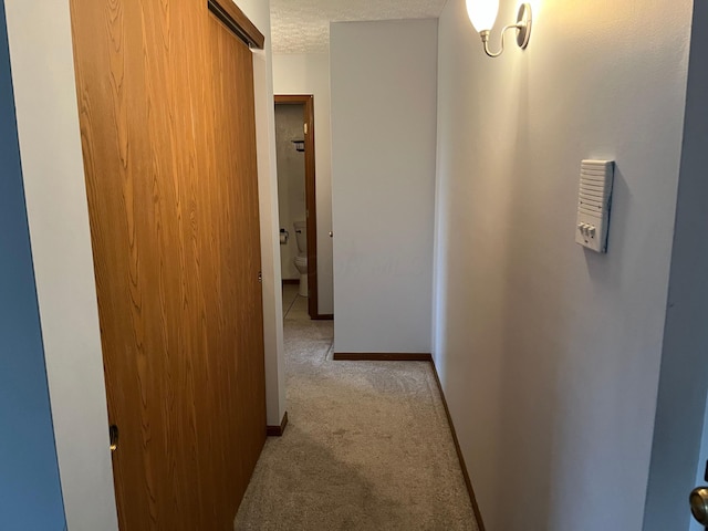 hallway with light colored carpet and a textured ceiling